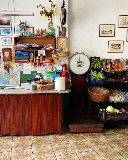 Indoor view of the interior of a shop featuring a wooden counter, shelves with various objects, and an assortment of fruits.