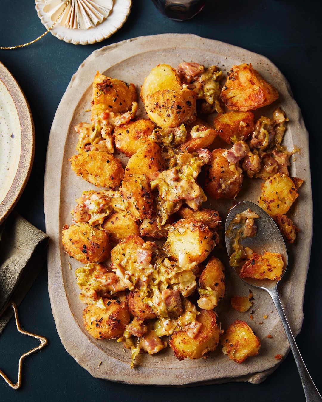 Overhead shot of golden brown potatoes with leeks and cream sauce served on a tan stoneware platter, a festive holiday food.