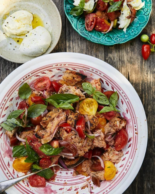 Overhead shot of Panzanella salad with tomatoes, onions, basil, bread cubes on a white patterned plate with wooden table backdrop.