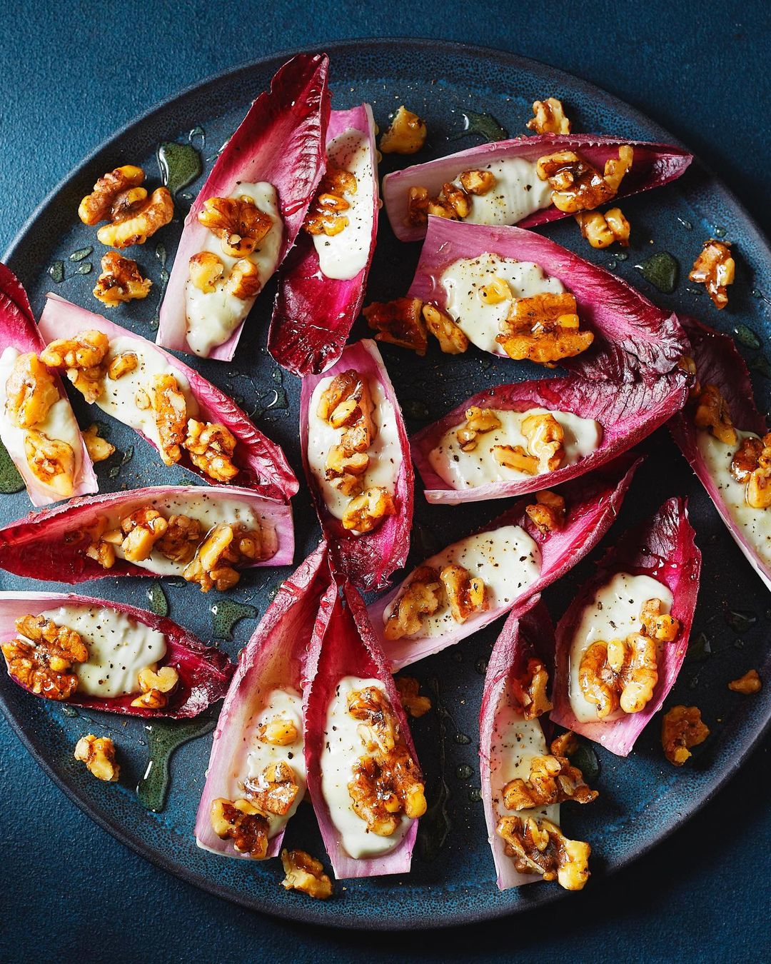 Overhead shot of a blue plate featuring endive leaves filled with a creamy topping and walnuts, styled with natural light.
