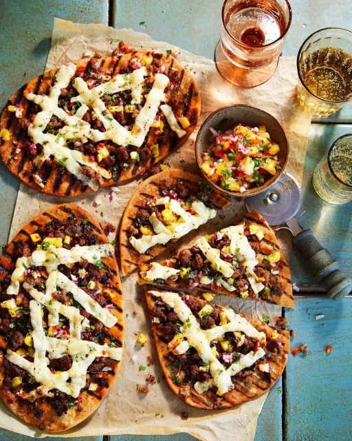 Flatbread pizzas with grilled marks, topped with cheese and savory ingredients next to a bowl of salsa and a couple of drinks.
