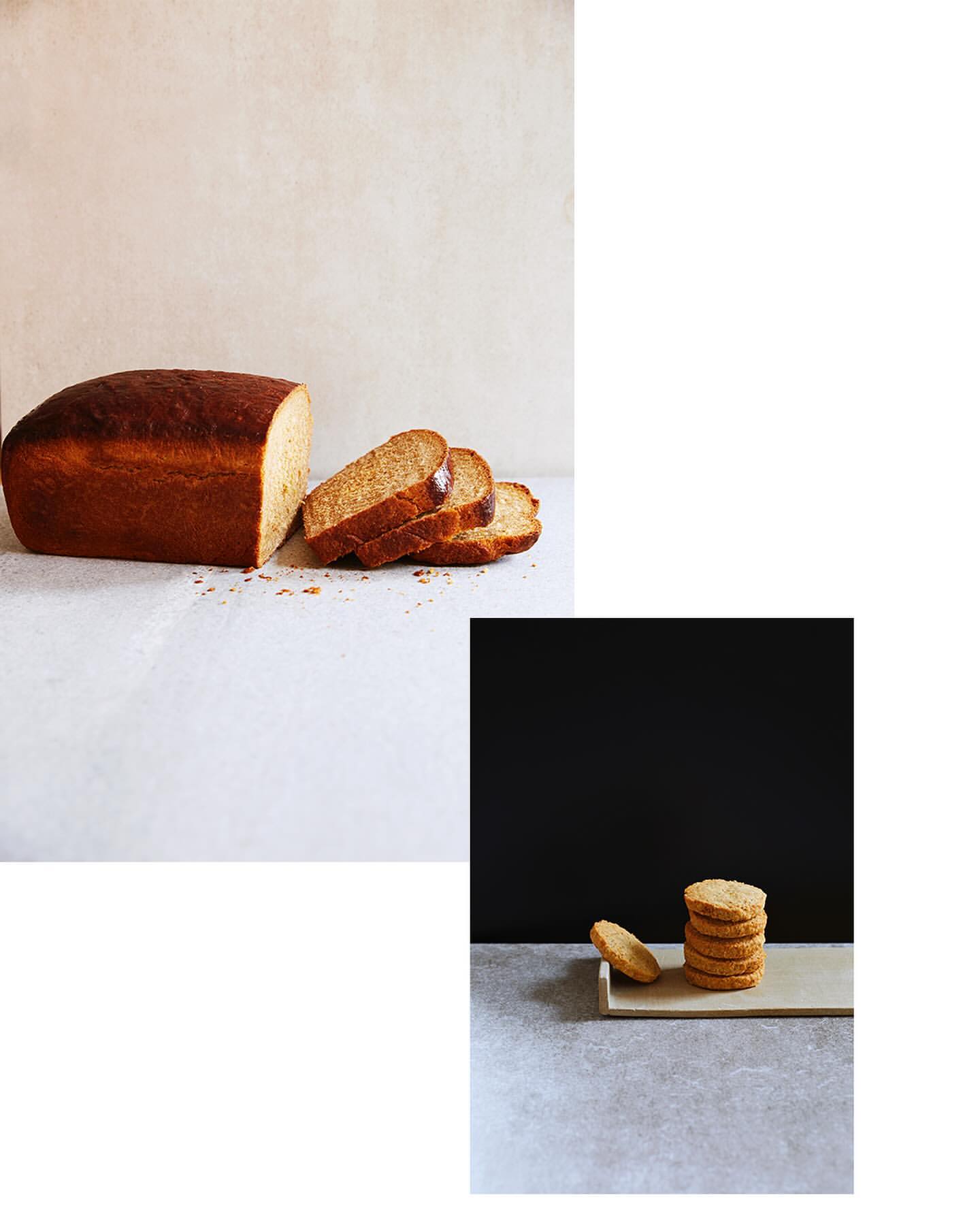 Studio shot of sliced loaf bread and stacked cookies on grey surface against muted beige and dark background. Food photography.