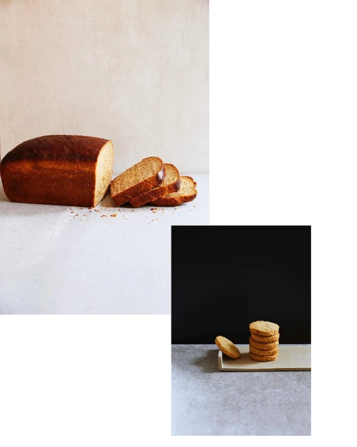 Studio shot of sliced loaf bread and stacked cookies on grey surface against muted beige and dark background. Food photography.