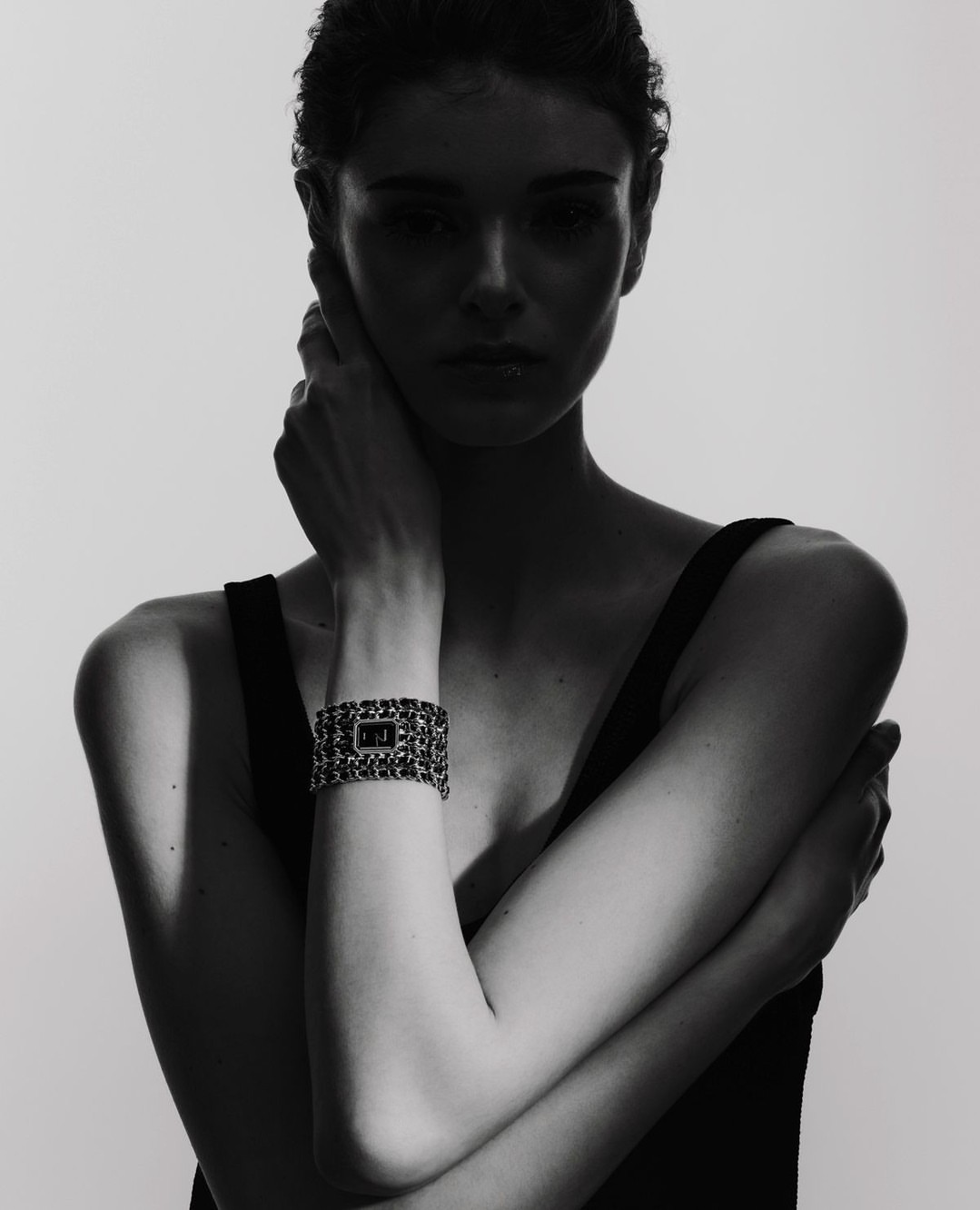 Close-up of a woman posing in a sleeveless top, wearing a chain-link bracelet watch, set against a solid white background.