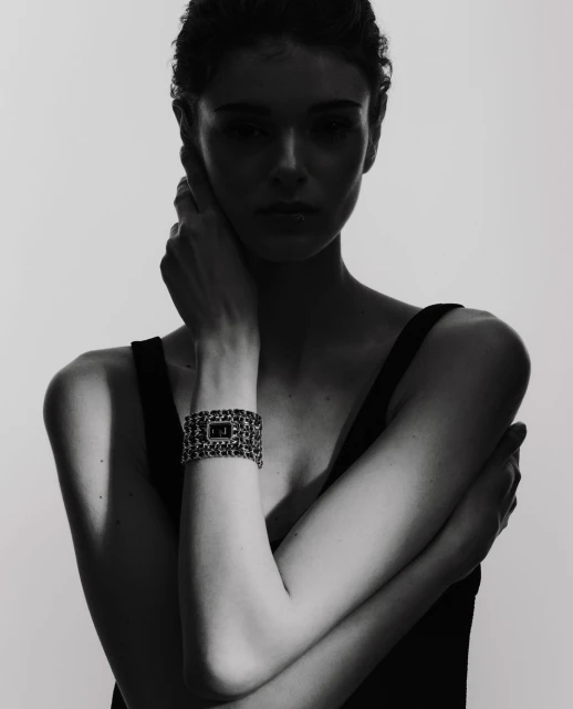 Close-up of a woman posing in a sleeveless top, wearing a chain-link bracelet watch, set against a solid white background.