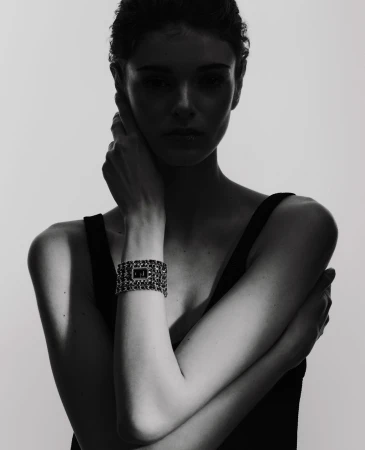 Close-up of a woman posing in a sleeveless top, wearing a chain-link bracelet watch, set against a solid white background.