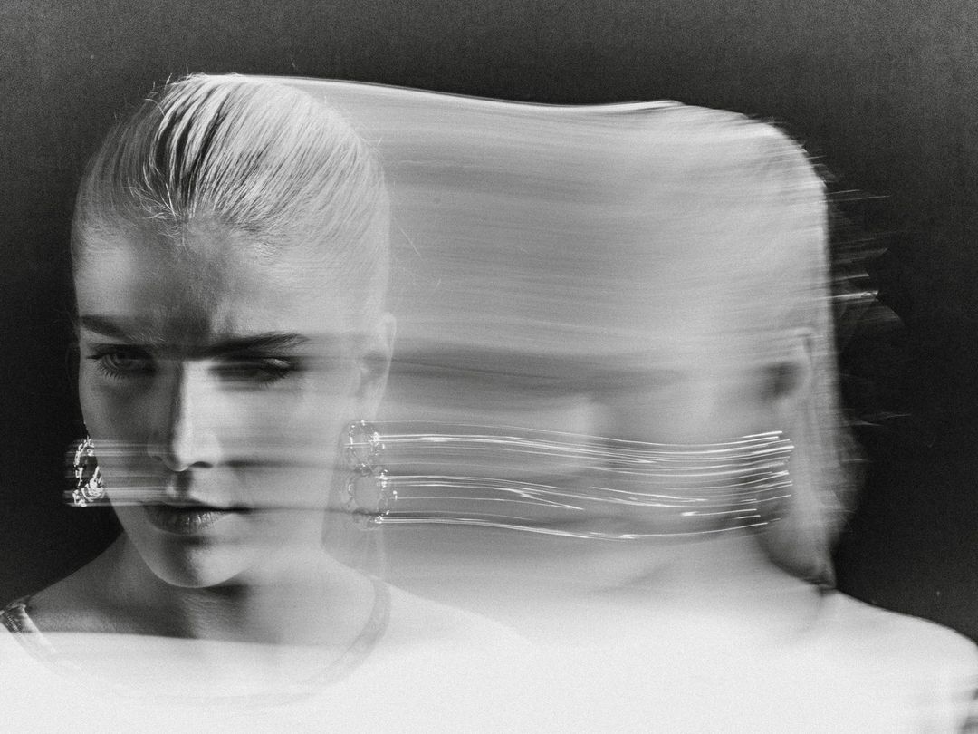 Monochrome portrait of a blonde woman with motion blur and light trails around her face, wearing earrings, against a dark background.