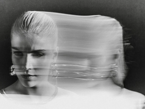 Monochrome portrait of a blonde woman with motion blur and light trails around her face, wearing earrings, against a dark background.