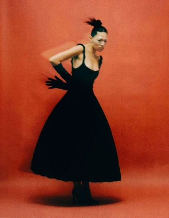 Elegant woman in black dress and gloves poses against a red studio backdrop in a fashion shot featuring motion blur.