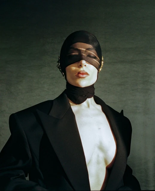 A woman wearing a black headscarf and blazer, eyes closed, in a dimly lit studio, fashion portrait, beauty shot, looking elegant and chic.