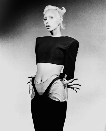 Monochrome portrait of a woman with short light hair and long dark fingernails wearing a cropped black top and dark skirt