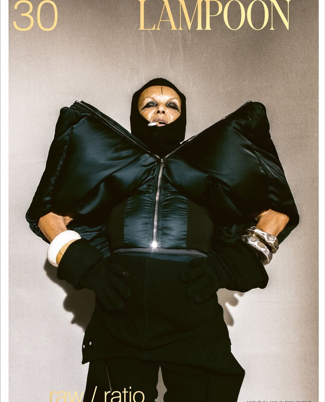 Androgynous person in a black puffer jacket and black pants poses in front of a grey backdrop for a fashion editorial magazine cover.
