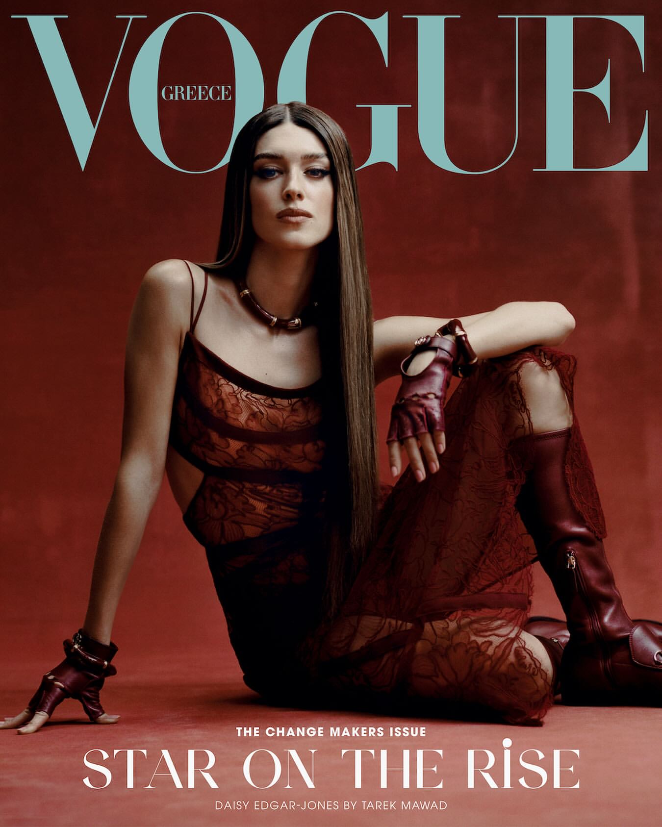 Vogue Greece cover featuring Daisy Edgar-Jones in a red lace dress and matching boots, posing against a reddish-brown backdrop.