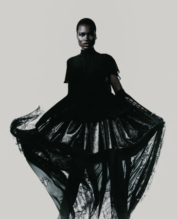 Black woman in a flowing dark lace dress standing against a seamless light background by photographer Tarek Mawad
