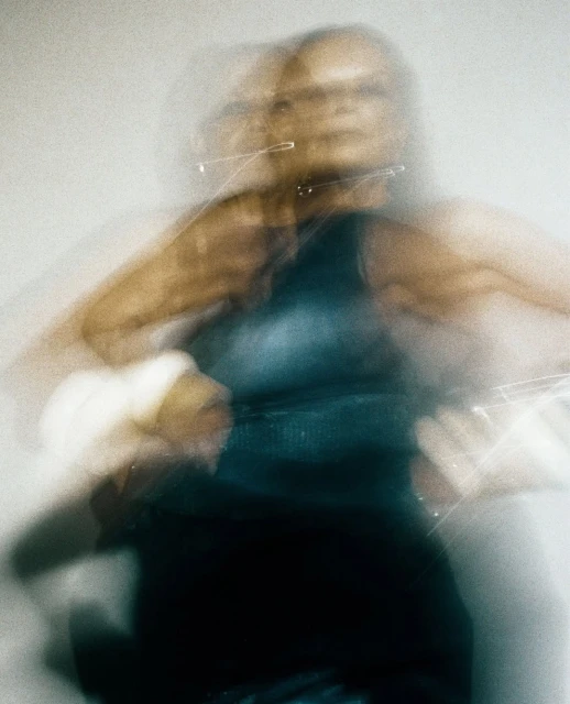 Abstract portrait of an adult female with blurred motion effect, wearing a dark top, against a neutral background.