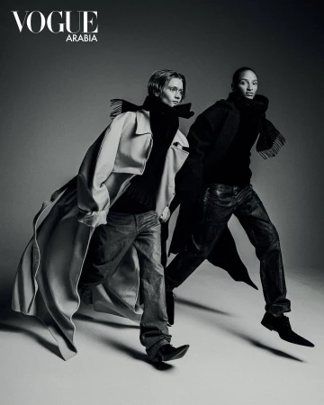 Monochrome fashion portrait of two models striding forward against a plain grey studio background.