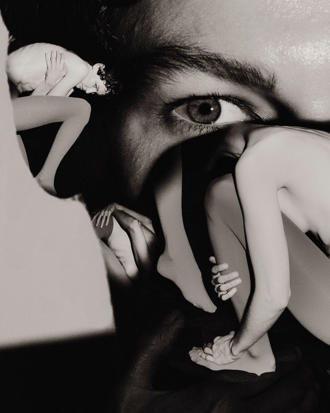 Monochrome collage featuring a close-up of a person's eye combined with multiple partial figures, creating a surreal and artistic effect.