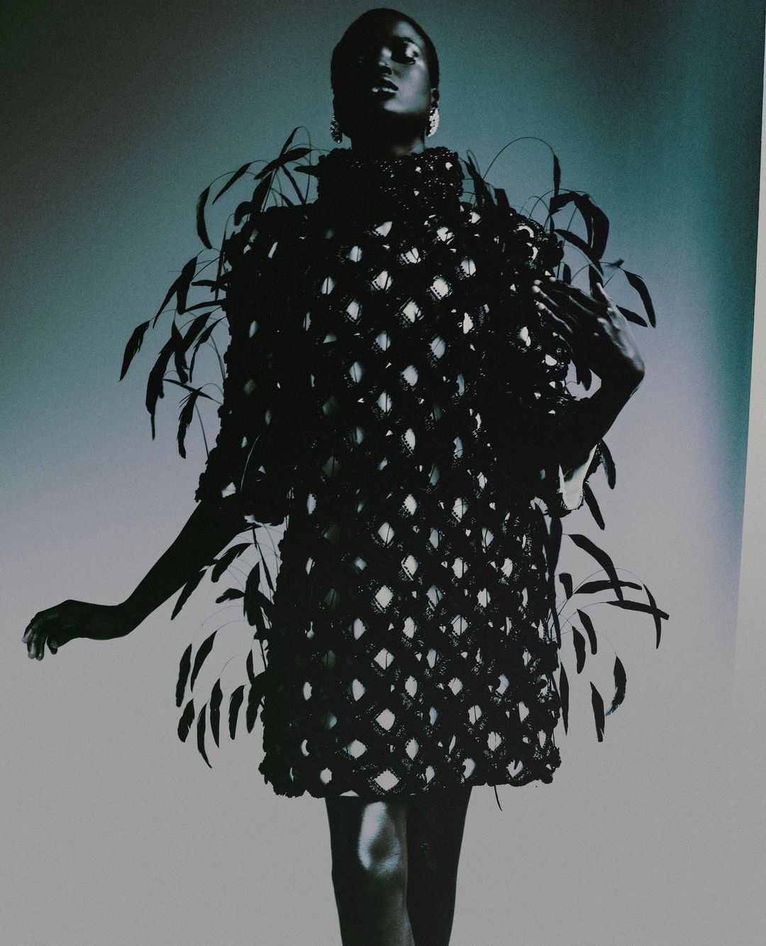 Fashion model wearing a black beaded and feathered dress, posing in a studio with a grey background. Haute couture concept.