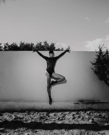 Monochrome full-length portrait of a dancer in a black bodysuit posing gracefully in front of an outdoor concrete wall.
