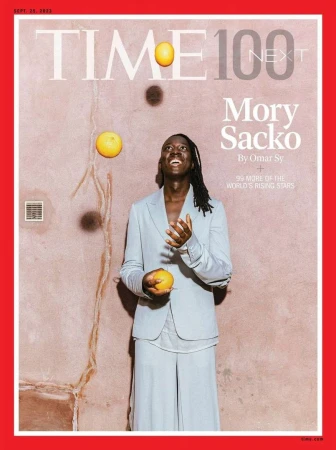 Magazine cover featuring Mory Sacko juggling oranges, wearing a light blue suit against a textured peach-colored background.