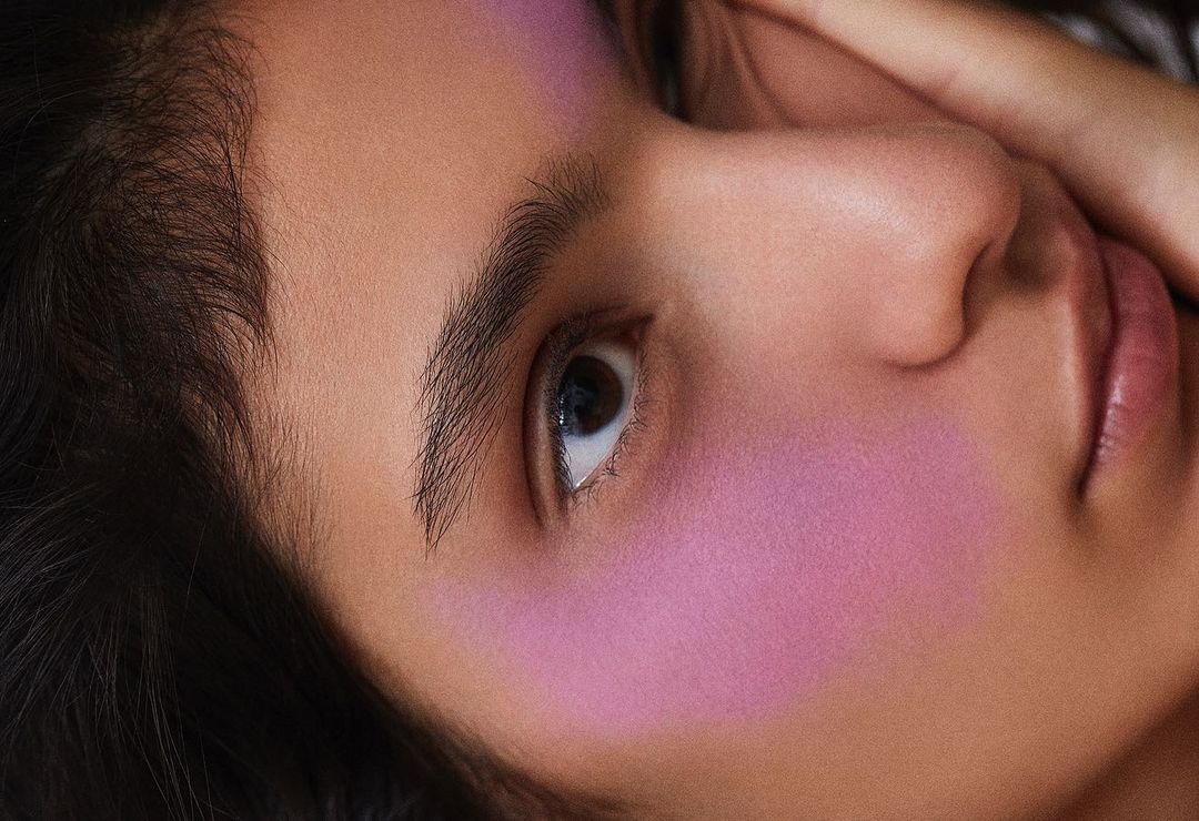 Close-up portrait of a model with vibrant purple blush and hand near face, photographed by Tassili Calatroni in Milan
