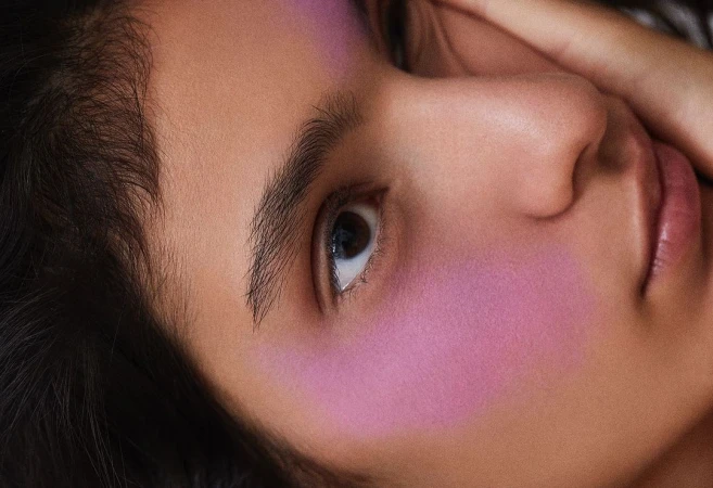 Close-up portrait of a model with vibrant purple blush and hand near face, photographed by Tassili Calatroni in Milan