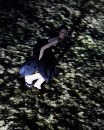 A woman in a dark dress captured with motion blur against a textured ground by Tassili Calatroni in Milan.