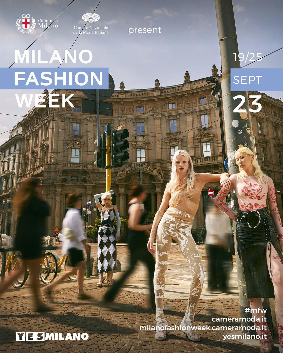 Two fashion models pose in front of a traffic light and historic building in Milan, Italy during Fashion Week. Pedestrians in motion.