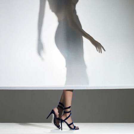 Fashion shot featuring woman's legs in blue stiletto heels against a graduated background with the blurry shadow of a figure above.