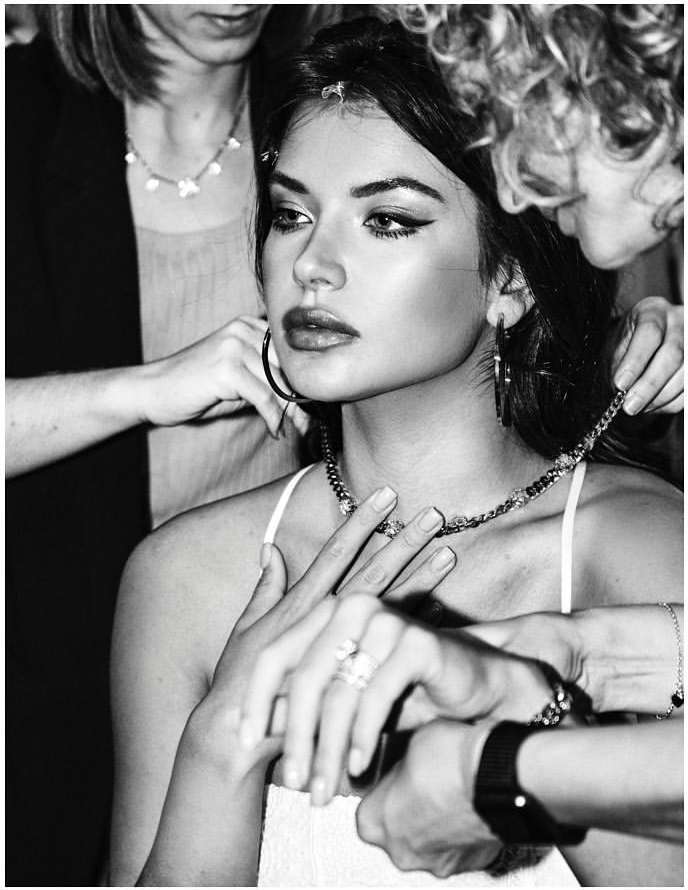 Black and white portrait of a young woman having jewelry put on by two other women; close-up shot capturing the fashion and beauty scene.