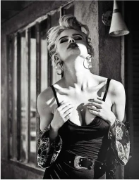Black and white portrait of a woman with blond hair wearing a dark top, large hoop earrings, and a belt, tilting her head back outdoors.