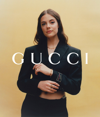 Brunette woman in a black cropped blazer and skirt poses against a yellow background with the Gucci logo superimposed on the image.