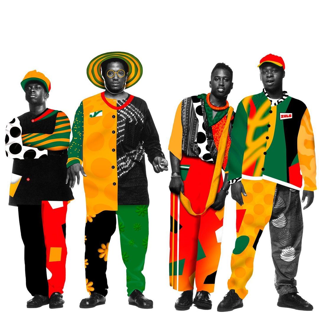 Four people stand against a white background, wearing brightly colored patchwork outfits and hats in hues of yellow, green, red, and black.