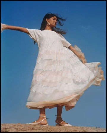 Model in a white pleated dress with arms outstretched against a bright blue sky by Tenzin Lhagyal