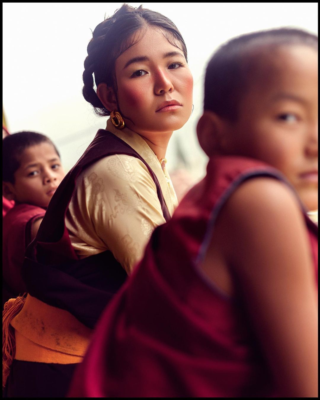 Portrait of a young woman with braided hair in traditional Asian clothing alongside children in robes, creating a culturally rich scene.