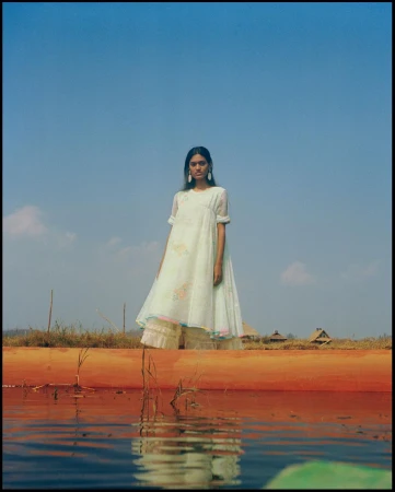 South Asian woman standing on a wooden boat in a light-coloured embroidered dress against a clear blue sky