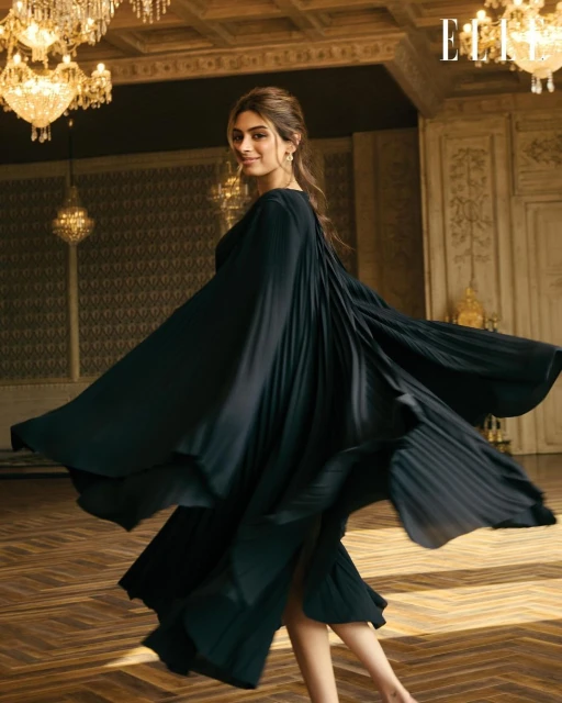 Elegant woman in flowing black dress twirling in a grand hall beneath chandeliers. Fashion editorial shot for Elle magazine.