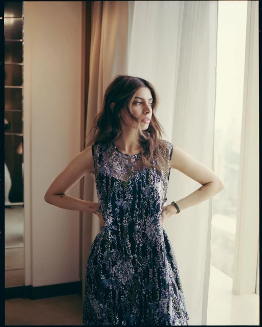 Indoor portrait of a woman in a floral dress looking towards a window, with neutral walls and soft, diffused lighting creating a serene atmosphere.