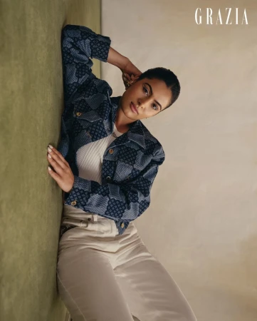 Woman in patterned blue jacket and white pants posing against a textured wall by photographer Tenzin Lhagyal