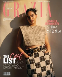 Woman in patterned skirt and textured top posing against a plain wall with harsh sunlight casting shadows