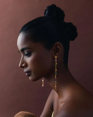 Profile portrait of a South Asian woman wearing long gemstone drop earrings and styled hair by Tenzin Lhagyal