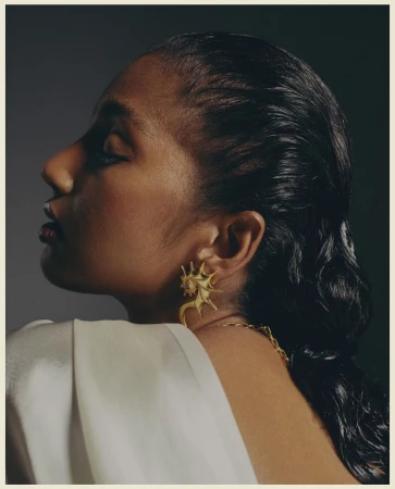 Profile portrait of a woman wearing a gold seashell earring and white draped top by Tenzin Lhagyal