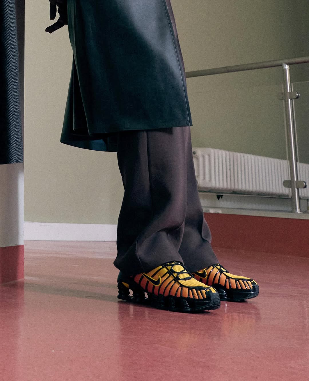 Stylish athletic shoes in yellow and black are prominently featured, worn with dark trousers and a black jacket indoors.