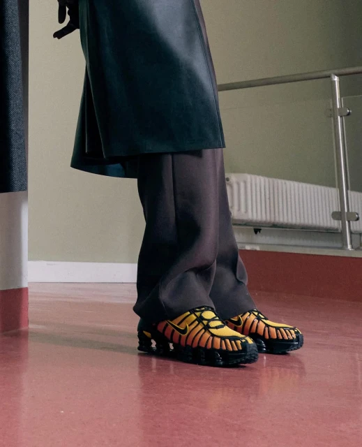 Stylish athletic shoes in yellow and black are prominently featured, worn with dark trousers and a black jacket indoors.