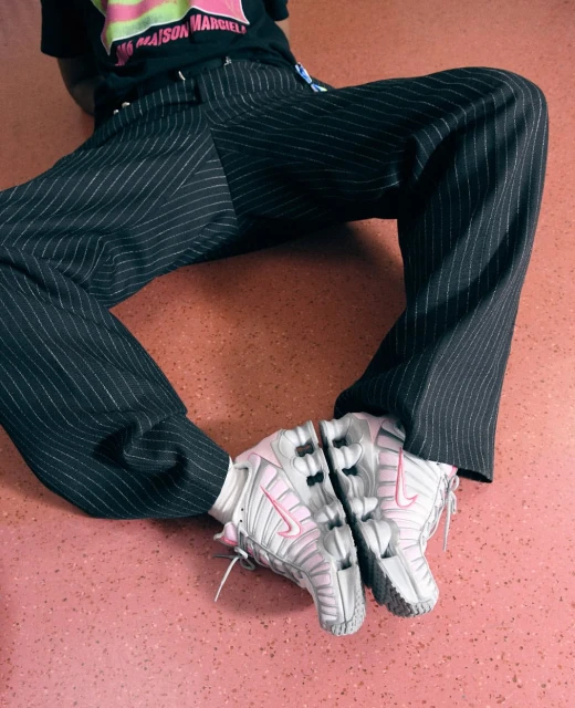 Close-up shot of a person wearing pinstripe pants and pink and white sneakers, sitting on a peach colored surface.