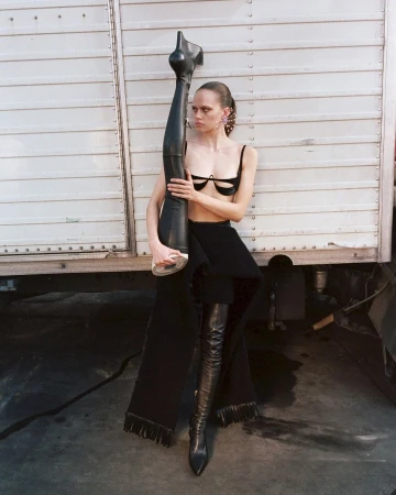 Model holding a giant leather boot while posing against a corrugated metal truck wall in Milan by Teresa Ciocia