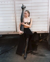 Model holding a giant leather boot while posing against a corrugated metal truck wall in Milan by Teresa Ciocia
