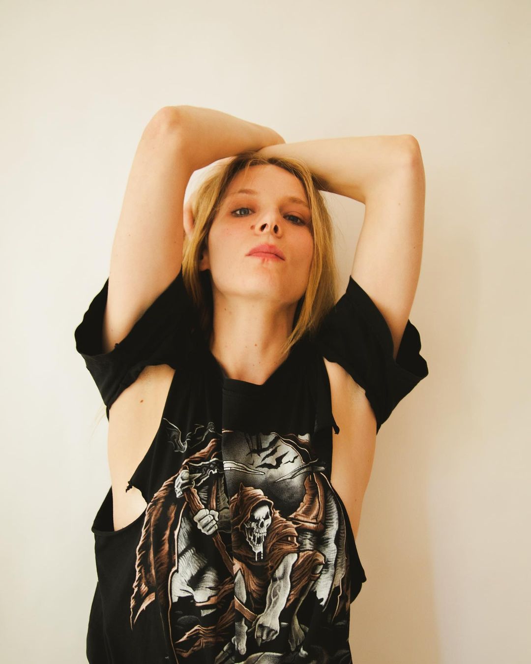 Woman in a black graphic t-shirt with arms raised overhead against a plain neutral background