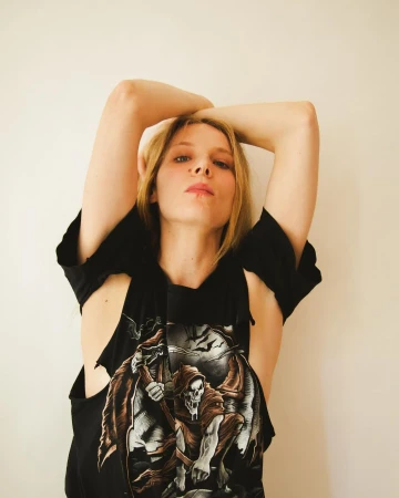 Woman in a black graphic t-shirt with arms raised overhead against a plain neutral background