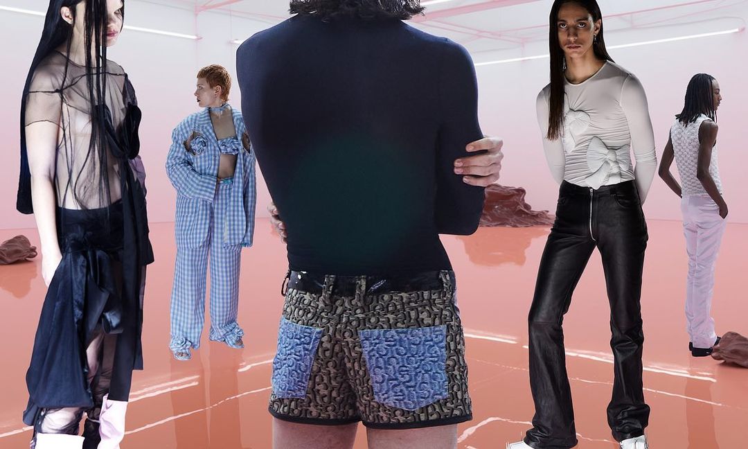Multiple gender-neutral fashion models strike poses in studio with diverse designs: sheer tops, patterned shorts, leather pants.